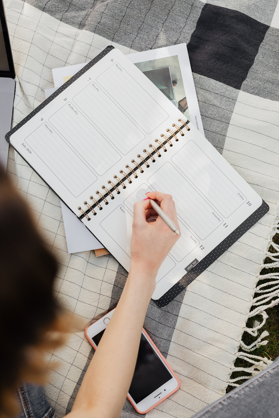 Student writing in organizer while sitting on picnic rug